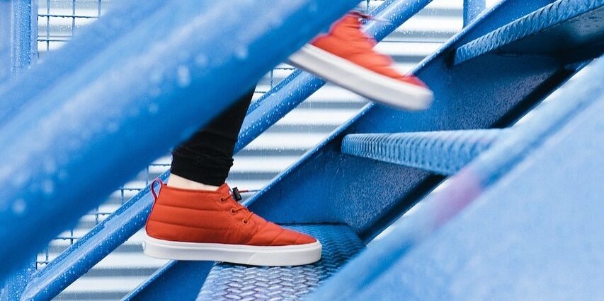 Close up on feet walking up blue steps in the rain in red trainers
